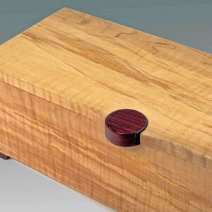 May include: A wooden box with a natural wood finish and a dark red wooden knob. The box has a simple design and is made of high-quality wood.