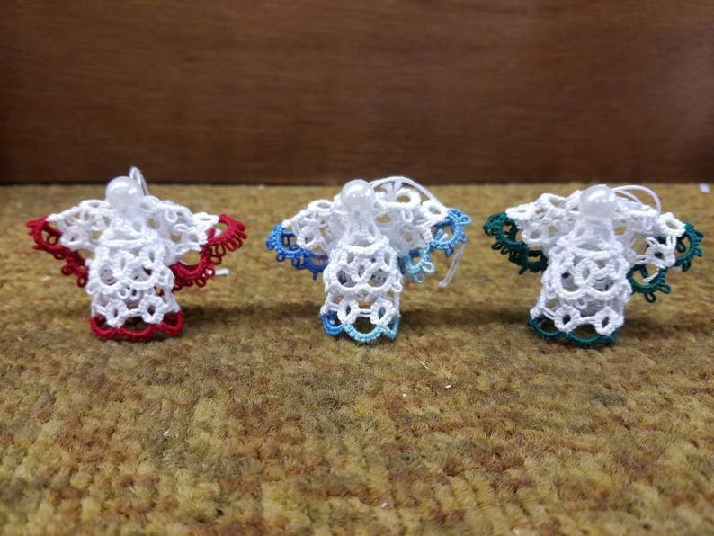 May include: Three white crocheted angel ornaments with red, blue, and green accents. The ornaments are hanging from a string.