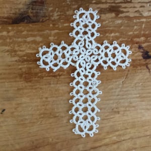May include: White crocheted cross with intricate detail, a delicate and handmade design.