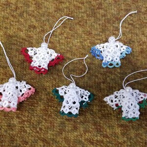 May include: Five white crocheted angel ornaments with different colored trim. The ornaments have a pearl bead at the top and are hanging from white string.