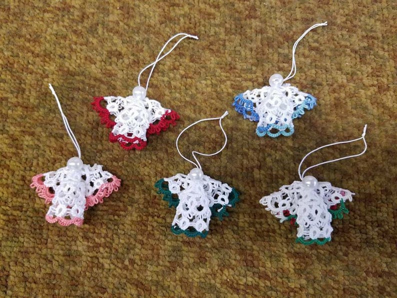 May include: Five white crocheted angel ornaments with different colored trim. The ornaments have a pearl bead at the top and are hanging from white string.