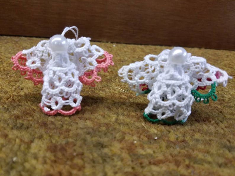 May include: Two white crocheted angel ornaments with pearl beads. One angel has pink trim and the other has green trim.