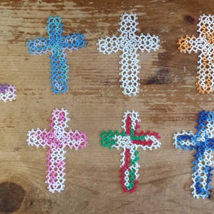 May include: Eight handmade crocheted crosses in various colors, including blue, purple, pink, green, and orange. The crosses are all the same size and shape, and they are arranged in a row on a wooden surface.