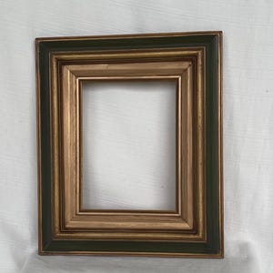 May include: A rectangular picture frame featuring a dark forest green outer border and a metallic gold inner border. The frame has a stepped, multi-layered profile with a deep recessed center, showcasing a classic design with clean, sharp edges.