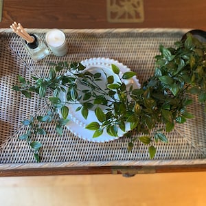 May include: A woven wicker tray with a white plate and a small potted plant. The tray is decorated with a white candle and a small bottle of essential oil.