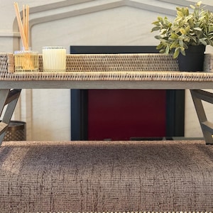 Puede incluir: Una mesa de bandeja de madera gris con una parte superior de mimbre tejido. La mesa está plegada y tiene dos patas a cada lado. La mesa está sobre una alfombra marrón.