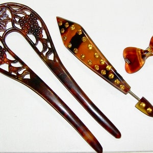 Peut inclure: Ensemble de trois peignes à cheveux en écaille de tortue. Un peigne présente un motif de vigne, un autre est un peigne simple et pointu avec des accents dorés, et le troisième est un peigne en forme de nœud.