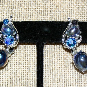 Puede incluir: Un par de pendientes de plata con una perla negra en forma de lágrima y detalles de cristal azul.