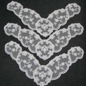 May include: Three white lace appliques with a scalloped edge and floral embroidery. The appliques are arranged in a layered pattern, showcasing their delicate design. Ideal for crafting or embellishing garments.