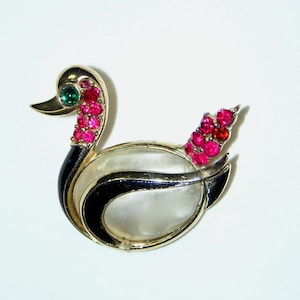 Op de afbeelding: Een vintage eendenbroche met een goudkleurig metalen frame. De eend heeft een parelmoer lichaam, zwarte accenten en een groene edelsteen oog. De nek en staart zijn versierd met roze en rode strass.