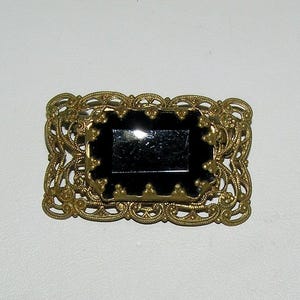 May include: A gold filigree brooch with a black glass center.