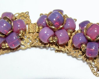 May include: Vintage bracelet featuring clusters of lavender-colored beads with a gold-tone filigree setting. The beads have a slight iridescent quality, and the bracelet has a chain closure. A classic piece of jewelry.