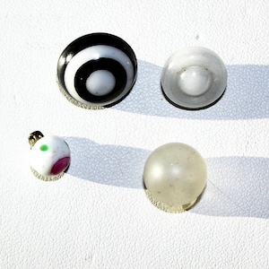 May include: Four different round buttons. One button is black and white with concentric circles. One button is white with a small circle in the center. One button is white with pink and green dots. One button is white and translucent.
