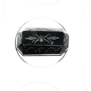May include: A black button with a gold and silver design. The button has a hole in the center.