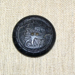 May include: A black button with a raised design of a person riding a horse. The button is round and has a smooth surface.