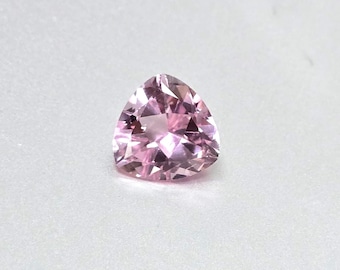 May include: A faceted, light pink gemstone with a triangular shape. The gem has multiple facets that reflect light, creating a sparkling effect. The stone is set against a white background.