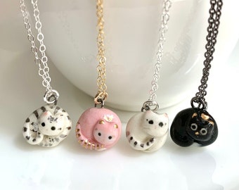May include: Four necklaces with ceramic cat pendants. The cats are curled up in a sleeping position. The necklaces are silver, gold, silver, and black.