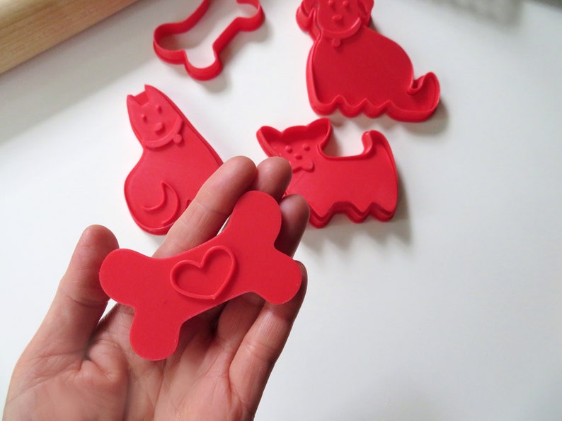 May include: A set of red plastic cookie cutters shaped like a bone with a heart, a dog, and a cat.