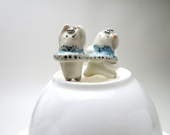 Puede incluir: Dos figuritas de cerámica blanca de gatos con tutús azules y plateados. Los gatos están de pie sobre un cuenco de cerámica blanca.