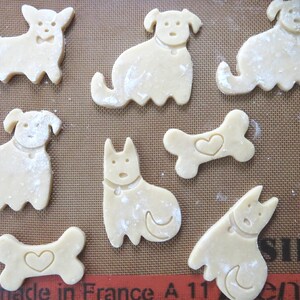 May include: A baking sheet with nine unbaked dog-shaped and bone-shaped sugar cookies. The cookies are dusted with flour and have heart-shaped cutouts.