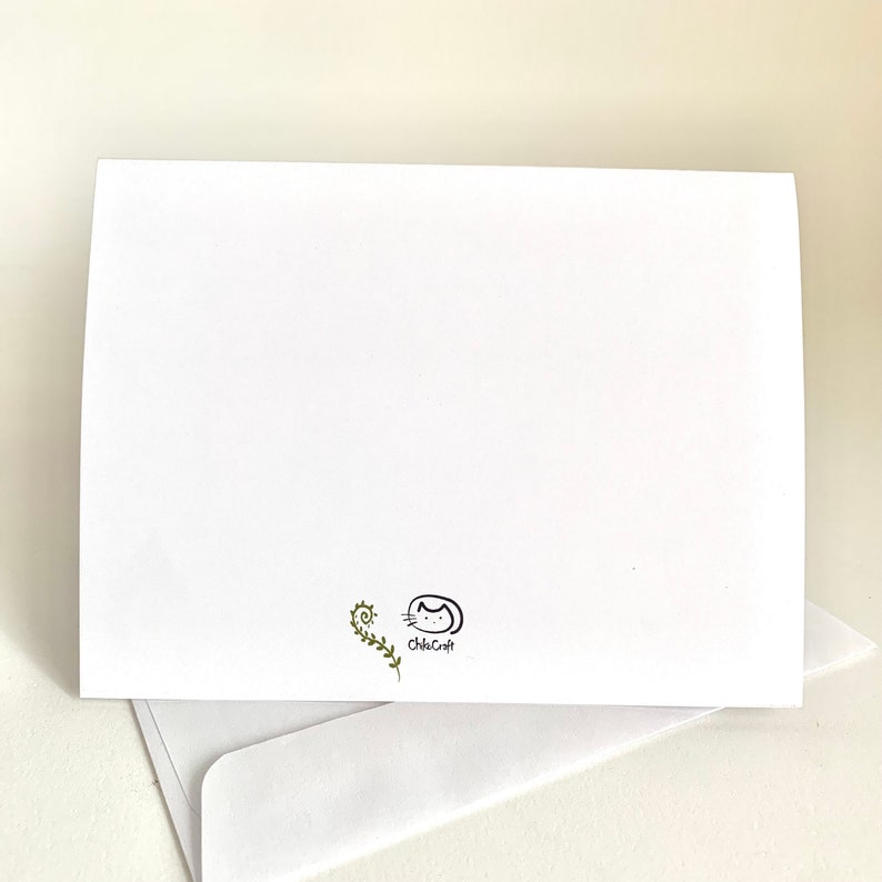 Op de afbeelding: Lege blanco kaart met een kleine groene wijnstok en een zwart-witte illustratie van een kat met de tekst "chicacat" eronder.