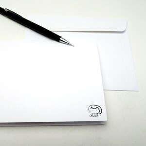 May include: A blank white card with a small black cat logo that says "ChicCraft" in the bottom right corner. A black pencil is lying on top of a white envelope.
