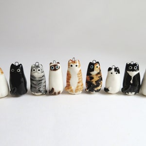 May include: A set of nine ceramic cat charms, each with a different color and pattern. The charms are all in a sitting position and have black eyes. They are perfect for adding a touch of whimsy to your jewelry or crafts.
