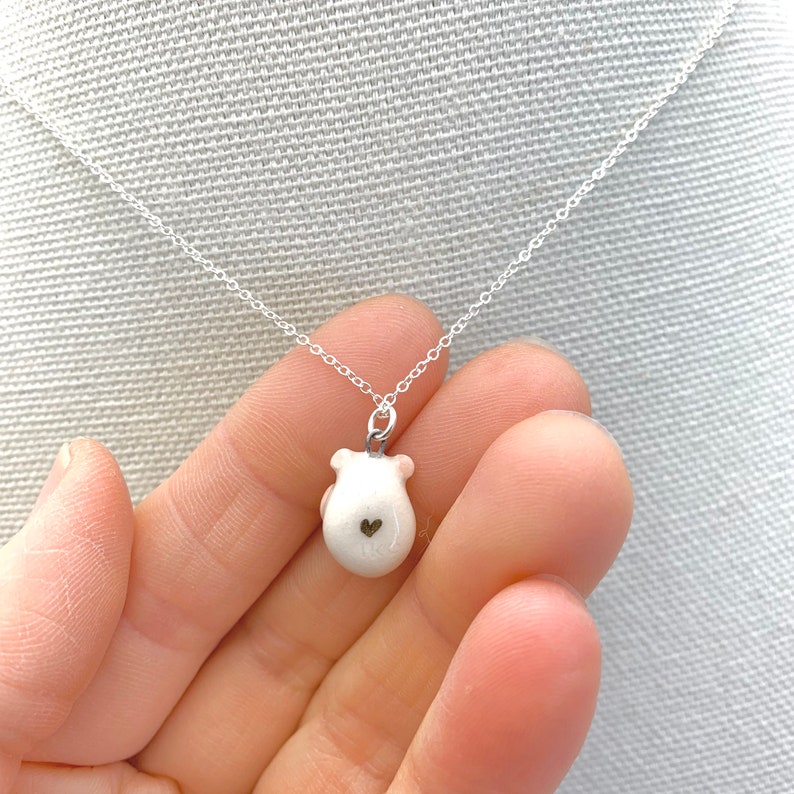 May include: A silver chain necklace with a white ceramic pendant shaped like a mouse with a small gold heart on its back.