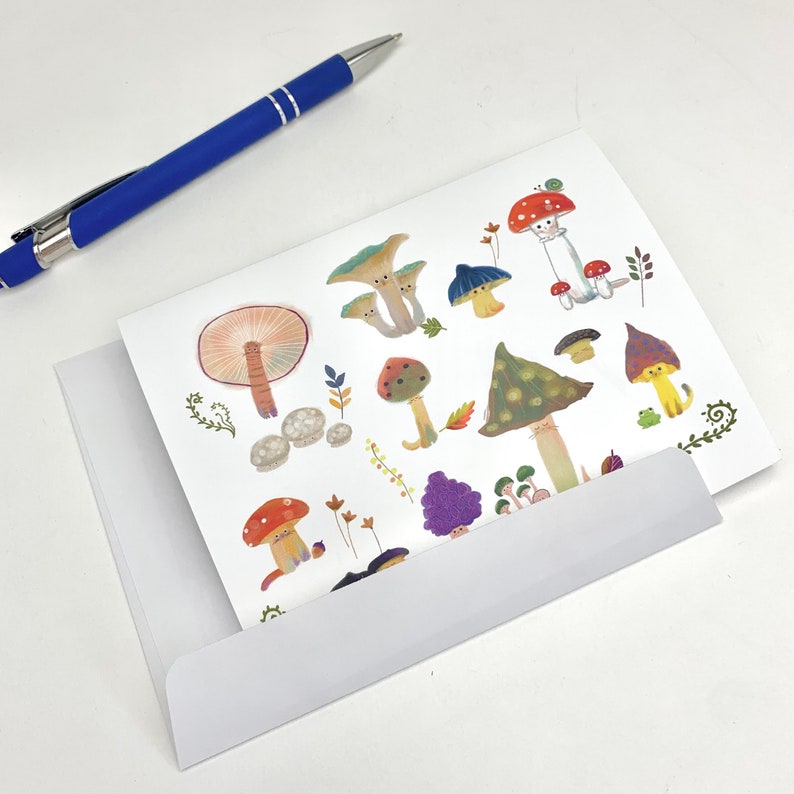 Op de afbeelding: Een witte kaart met een kleurrijke illustratie van verschillende paddenstoelen en een slak. De paddenstoelen zijn in verschillende vormen en maten, sommige hebben rode, oranje, gele, groene, paarse en bruine hoeden. Sommige paddenstoelen hebben witte vlekken en sommige hebben een witte steel. De slak zit op een rode paddenstoel.