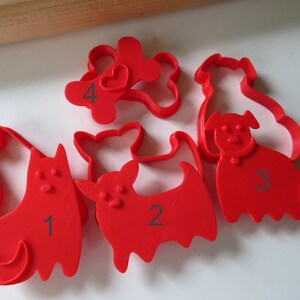 May include: Set of five red plastic cookie cutters shaped like dogs and a bone. The cutters are numbered 1 through 4.