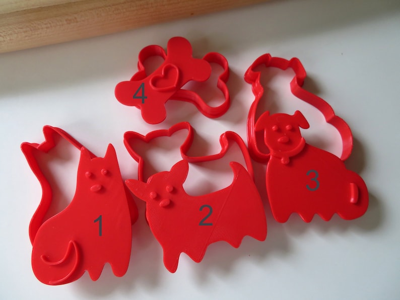 May include: Set of five red plastic cookie cutters shaped like dogs and a bone. The cutters are numbered 1 through 4.