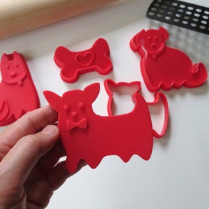 May include: Set of five red plastic cookie cutters shaped like dogs and a bone. The bone cutter has a heart in the center.