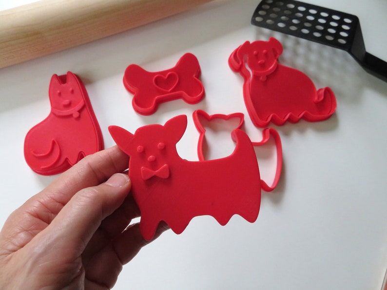 May include: Set of five red plastic cookie cutters shaped like dogs and a bone. The bone cutter has a heart in the center.