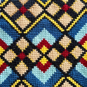 May include: A needlepoint embroidery textile featuring a repeating geometric pattern of diamonds and squares. The design incorporates a vibrant color palette of navy blue, light blue, beige, bright yellow, and deep red stitched in a grid.