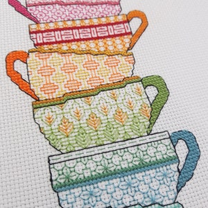 Puede incluir: Una pila de cinco tazas de t&eacute; de colores con diferentes dise&ntilde;os de patrones. Las tazas est&aacute;n apiladas de la m&aacute;s grande a la m&aacute;s peque&ntilde;a, con la taza superior de color rosa y la taza inferior de color verde.