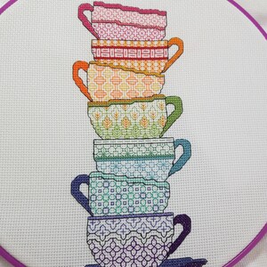 Puede incluir: Una pila de seis tazas de t&eacute; de colores con diferentes dise&ntilde;os de patrones. Las tazas est&aacute;n apiladas en un orden de arco&iacute;ris, de rosa a morado.