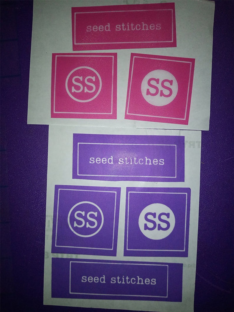 May include: Four labels with the text "seed stitches" and the initials "SS" in a circle. Two labels are pink with white text and initials, and two labels are purple with white text and initials.