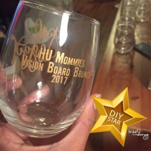 Puede incluir: Una copa de vino de vidrio transparente con letras doradas que dicen "TopkHU Mommies Vision Board Brunch 2017". Una estrella dorada con el texto "DIY STAR" est&aacute; en la esquina inferior derecha de la imagen.