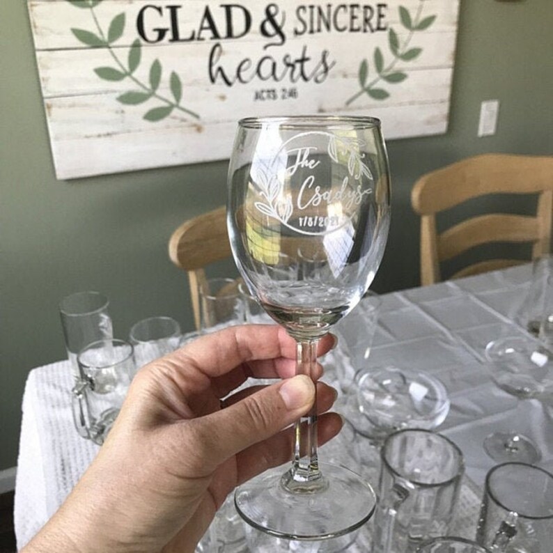 Puede incluir: Una copa de vino de vidrio transparente con tallo y base redonda. La copa est&aacute; grabada con el texto "The Craddocks 1/16/2021" dentro de un c&iacute;rculo.