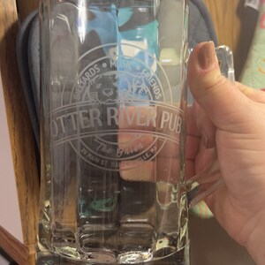 Puede incluir: Una jarra de cerveza de vidrio transparente con un dise&ntilde;o esmerilado que presenta el texto "Otter River Pub" y "The Onion" con un gr&aacute;fico de una nutria. El texto tambi&eacute;n incluye "Billiards Music Friends" y "29 Main St. Baldwinville, MA".