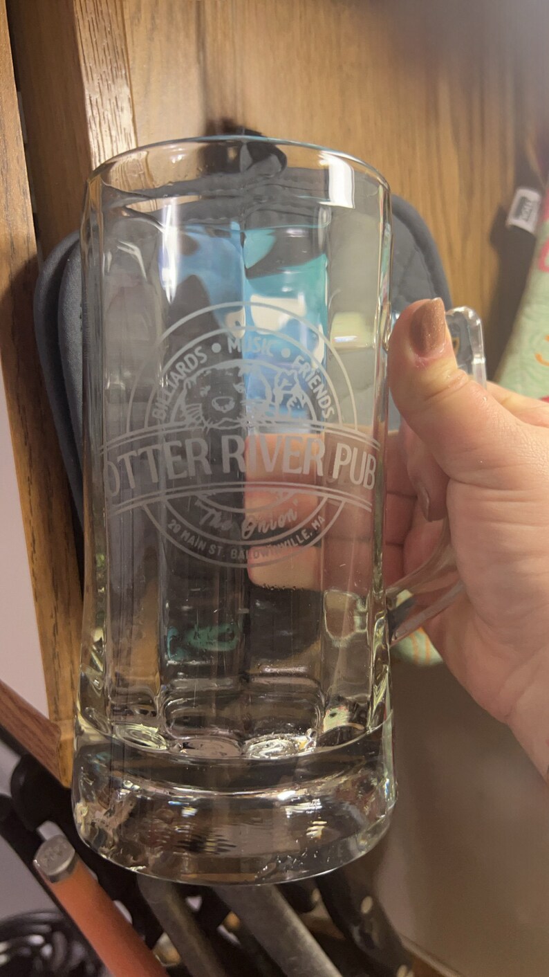 Puede incluir: Una jarra de cerveza de vidrio transparente con un dise&ntilde;o esmerilado que presenta el texto "Otter River Pub" y "The Onion" con un gr&aacute;fico de una nutria. El texto tambi&eacute;n incluye "Billiards Music Friends" y "29 Main St. Baldwinville, MA".