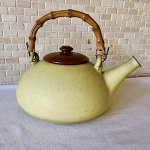 May include: A light green ceramic teapot with a brown lid and a bamboo handle. The teapot has a speckled finish and a rounded body.