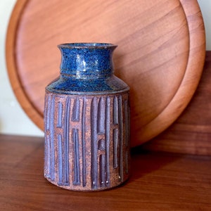 May include: A blue and brown ceramic vase with a textured design. The vase is sitting on a wooden surface.