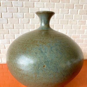 May include: A round, green ceramic vase with a mottled glaze. The vase has a narrow neck and a wide, rounded base.