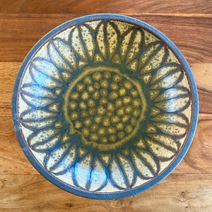 May include: A ceramic bowl with a sunflower design. The bowl is brown and blue with a textured surface. The sunflower design is in shades of brown and yellow.