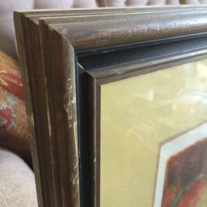 May include: A close-up of a dark brown wooden picture frame with a black inner border. The frame has a slightly distressed look with some scratches and wear. The matting is a light cream color.