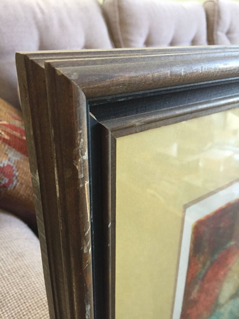 May include: A close-up of a dark brown wooden picture frame with a black inner border. The frame has a slightly distressed look with some scratches and wear. The matting is a light cream color.