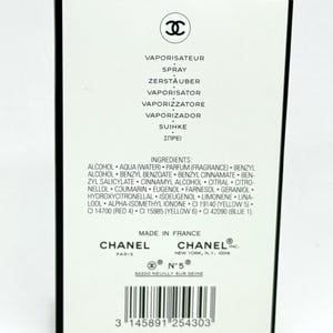 May include: A rectangular white perfume box with black trim featuring the Chanel logo at the top. The text includes the word spray in multiple languages, a detailed list of ingredients, the Chanel Paris and New York addresses, and a barcode.