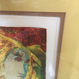 May include: A framed abstract print of a woman's face in a colorful, textured style. The colors are mostly yellow, red, green, and blue.