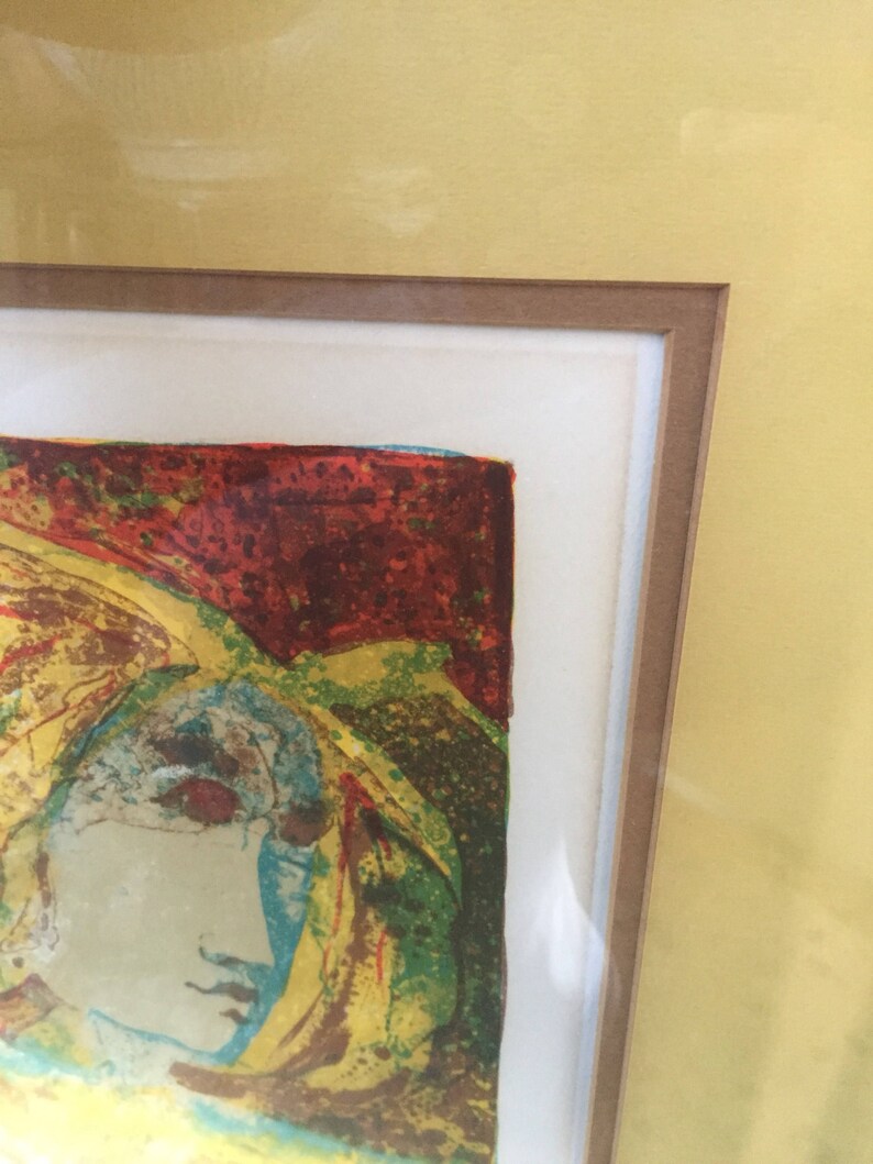 May include: A framed abstract print of a woman's face in a colorful, textured style. The colors are mostly yellow, red, green, and blue.